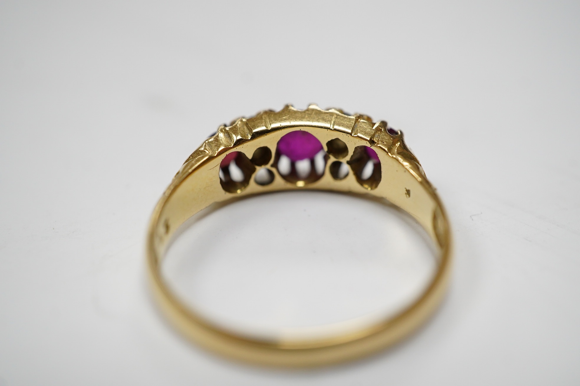 A George V 18ct gold and three stone ruby set half hoop ring, with diamond chip spacers, (one stone is probably a paste replacement), size O, gross weight 3.8 grams. Condition - poor to fair.